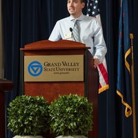 A man standing at a GVSU podium, speaking to the audience